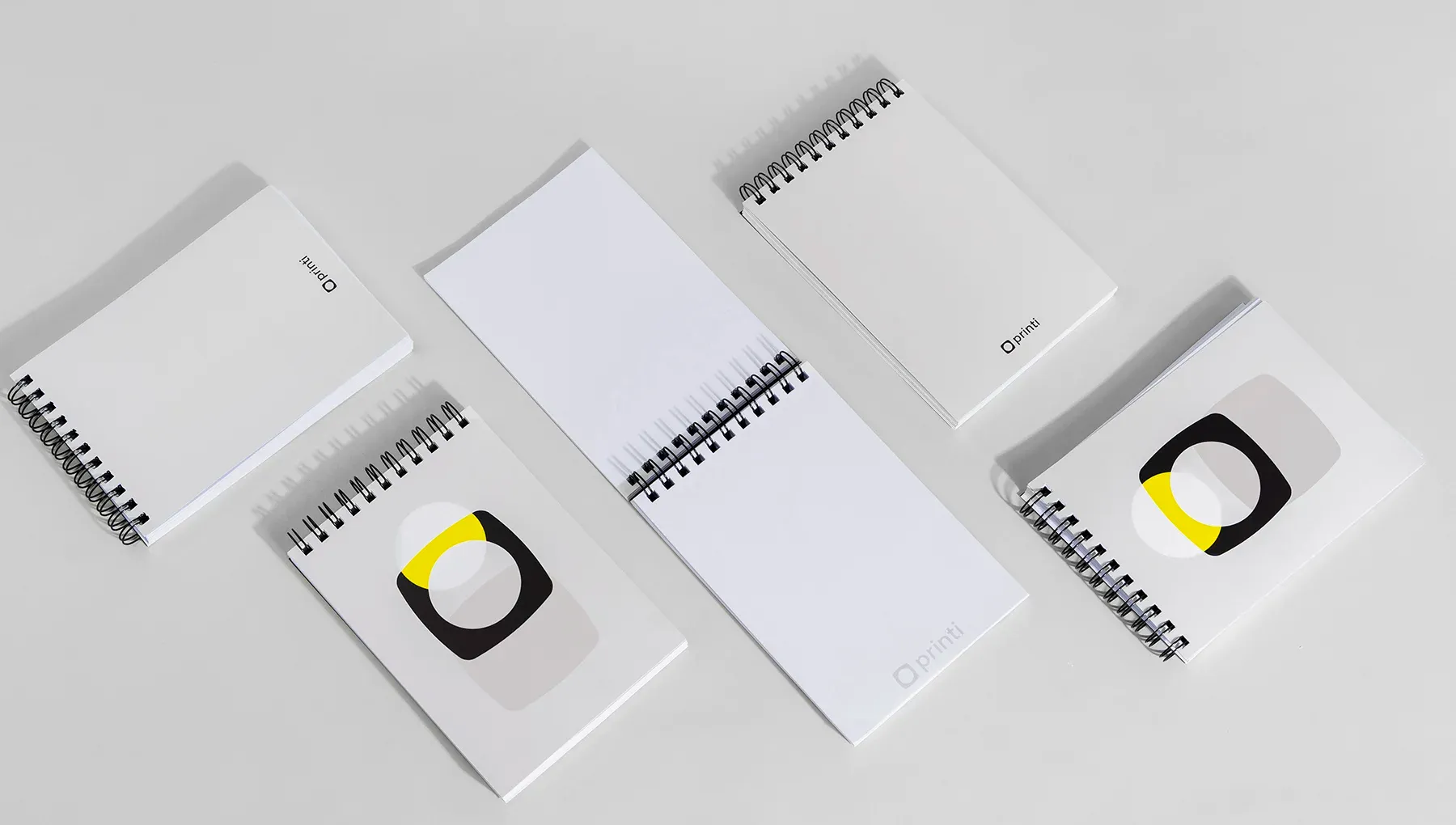 Diversas unidades de bloco de notas com capa wire-o espalhadas em ângulo, mostrando opções de capa personalizada e folhas internas brancas com o logotipo Printi.