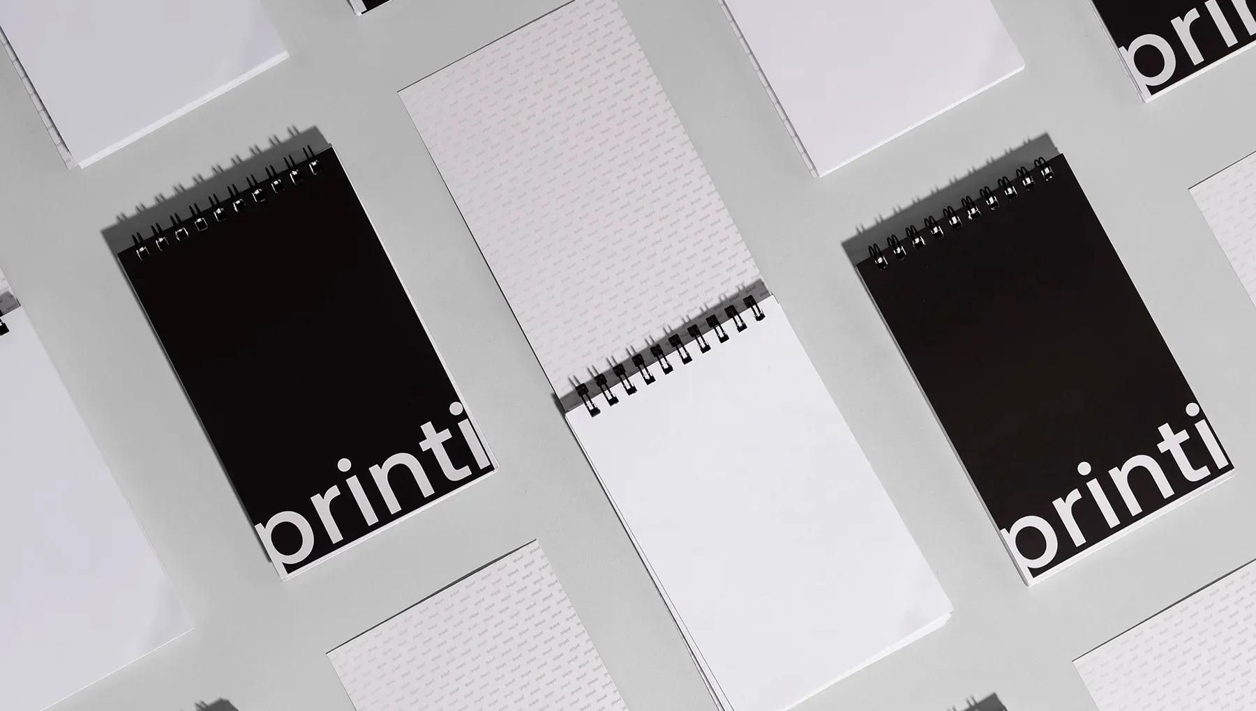 Vários modelos de bloco para rascunho com capa preta e marca Printi organizados em fundo cinza, mostrando folhas internas.